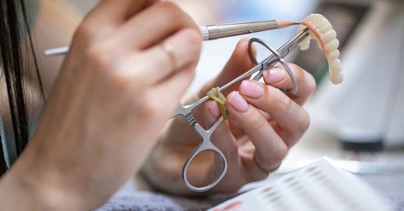 Manos trabajando con instrumental de precisión sobre una prótesis dental completa