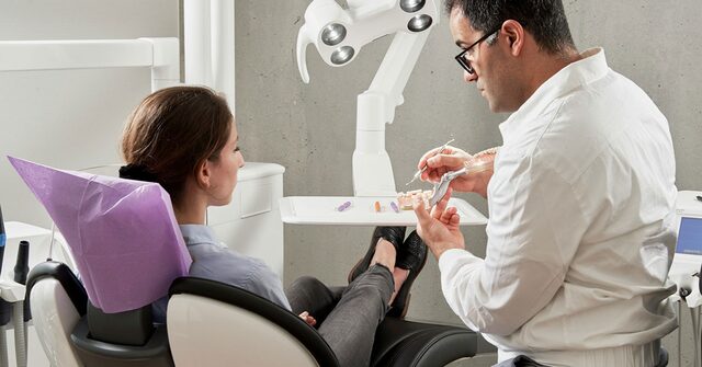 Odontólogo explicando un caso a una paciente sentada en el sillón dental