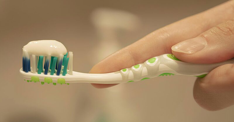 Mano sosteniendo un cepillo de dientes con pasta ante el espejo del baño