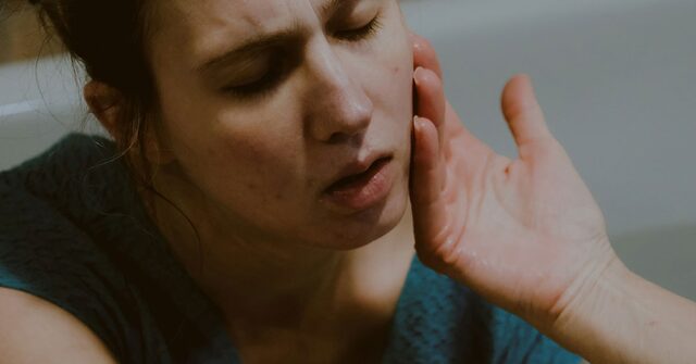 Mujer con gesto de dolor llevándose la mano a la mandíbula
